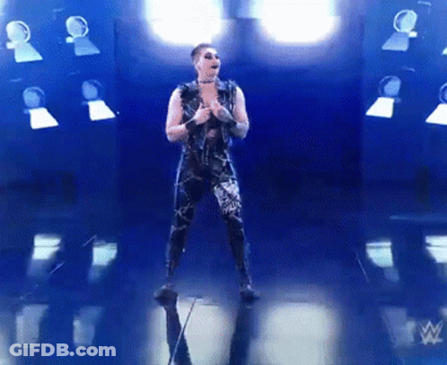 A Man In A Black Outfit Is Standing In Front Of A Wrestling Logo GIF