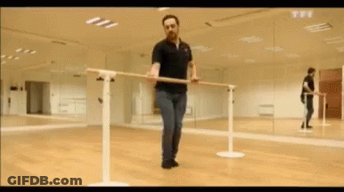 A Man In A Black Polo Shirt Is Holding A Bar In A Dance Studio . GIF