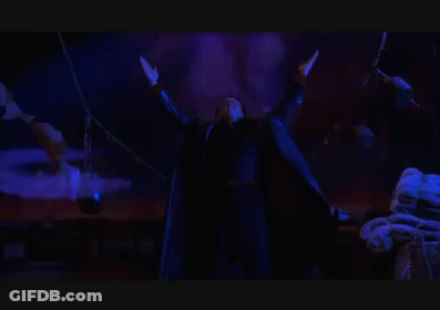 A Man In A Black Robe Is Standing In A Dark Room With His Arms Outstretched In Front Of A Group Of Bats . GIF