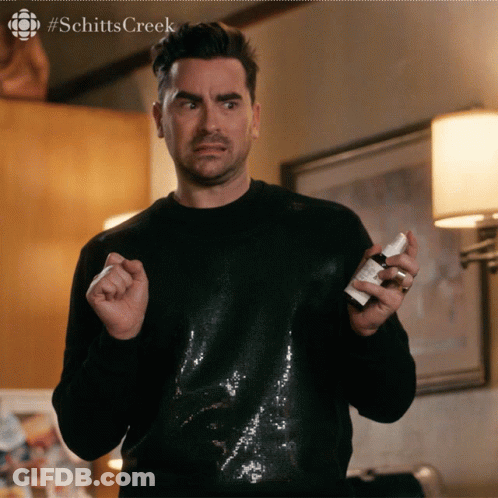 A Man In A Black Sequined Shirt Is Holding A Small White Bottle Of Something GIF