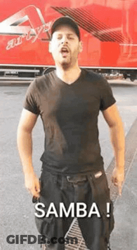 A Man In A Black Shirt And Black Pants Is Standing In Front Of A Red Truck And Singing . GIF