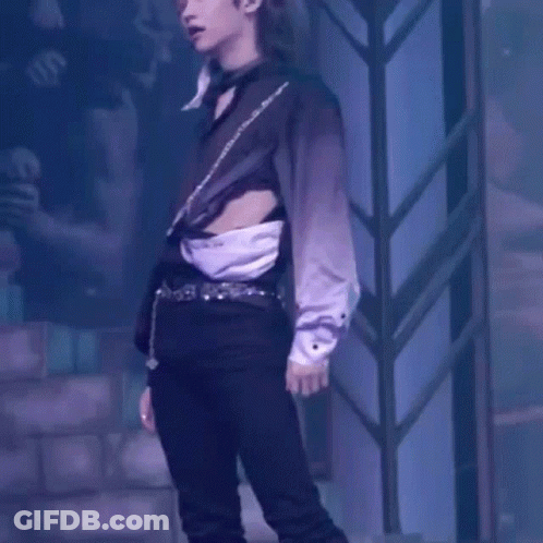 A Man In A Black Shirt And Black Pants Is Standing On A Stage With His Shirt Cut Off . GIF