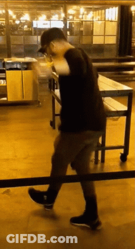 A Man In A Black Shirt And Black Shoes Is Walking Across A Wooden Floor GIF