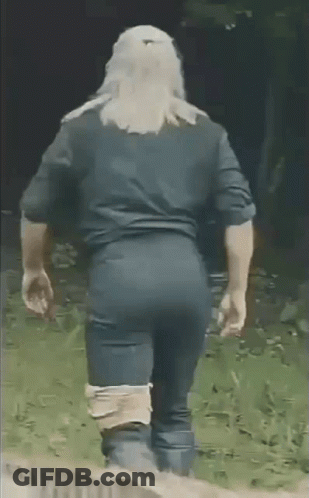 A Man In A Black Shirt And Blue Pants Is Walking In The Grass . GIF