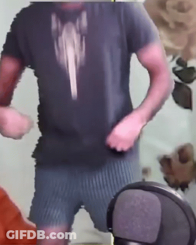 A Man In A Black Shirt And Blue Shorts Is Standing In Front Of A Microphone . GIF