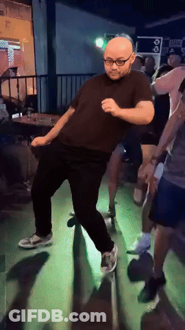 A Man In A Black Shirt And Glasses Is Dancing In A Dark Room GIF