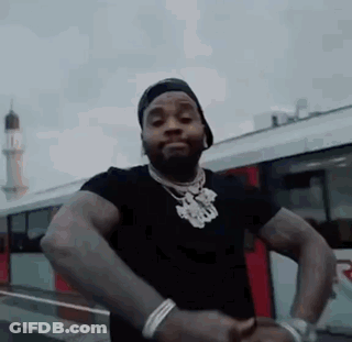 A Man In A Black Shirt And Hat Is Standing In Front Of A Bus . GIF