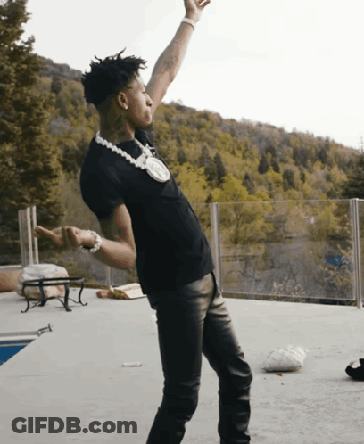 A Man In A Black Shirt And Leather Pants Is Standing On A Patio With His Arms In The Air GIF