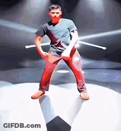 A Man In A Black Shirt And Red Pants Is Holding Two Sticks GIF