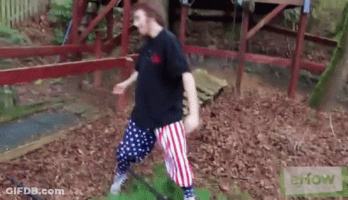 A Man In A Black Shirt And Red White And Blue Striped Pants Is Standing On A Grassy Field . GIF