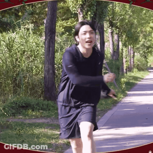 A Man In A Black Shirt And Shorts Is Running Down A Path In The Woods GIF