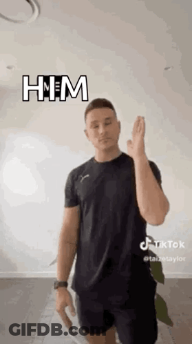 A Man In A Black Shirt And Shorts Is Standing In Front Of A White Wall And Giving A High Five . GIF