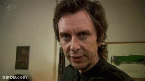 A Man In A Black Shirt And Tie Is Making A Funny Face In A Room . GIF