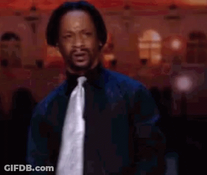 A Man In A Black Shirt And Tie Is Standing In Front Of A Crowd And Making A Funny Face . GIF