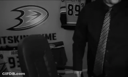 A Man In A Black Shirt And Tie Is Standing In Front Of A Wall That Says " Wasted " GIF