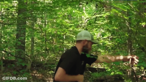 A Man In A Black Shirt And White Hat Is Walking Through The Woods . GIF