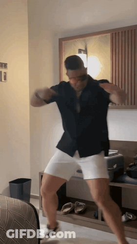 A Man In A Black Shirt And White Shorts Is Dancing In A Bedroom GIF