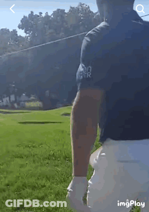 A Man In A Black Shirt And White Shorts Is Standing On A Golf Course Holding A Golf Club . GIF