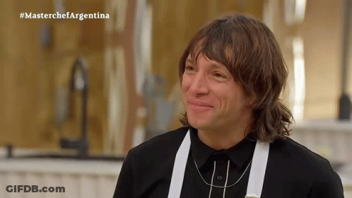 A Man In A Black Shirt And White Suspenders Is Smiling In Front Of A Masterchef Argentina Sign GIF