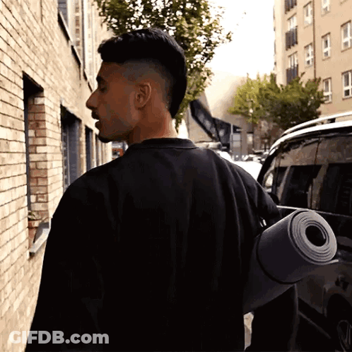 A Man In A Black Shirt Carrying A Yoga Mat On His Back GIF
