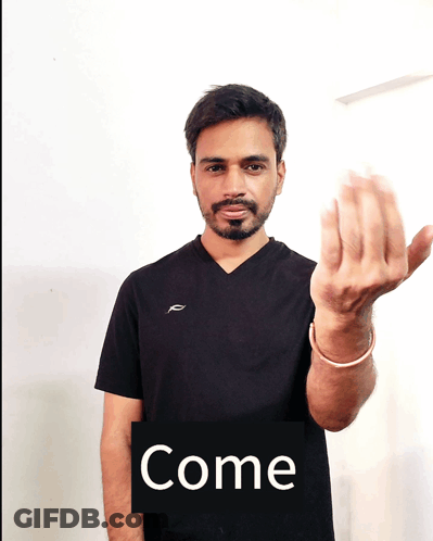 A Man In A Black Shirt Holds Up His Hand In Front Of A Sign That Reads Come GIF