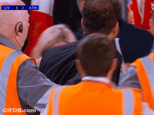 A Man In A Black Shirt Is Being Helped By A Man In An Orange Vest During A Liv 3 2 Atm Soccer Game GIF