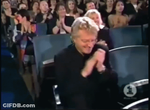 A Man In A Black Shirt Is Clapping In Front Of A Crowd With A Number 1 On Their Seat GIF
