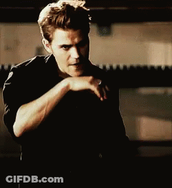 A Man In A Black Shirt Is Covering His Mouth With His Hand While Looking At The Camera . GIF