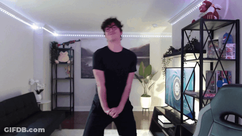 A Man In A Black Shirt Is Dancing In A Living Room With A Target On The Wall GIF