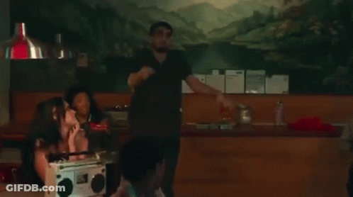 A Man In A Black Shirt Is Dancing In A Room With A Group Of People . GIF