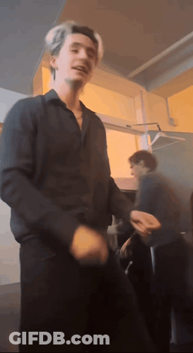 A Man In A Black Shirt Is Dancing In A Room With Other People GIF