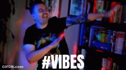 A Man In A Black Shirt Is Dancing In Front Of A Bookshelf With The Words #Vibes Above Him GIF