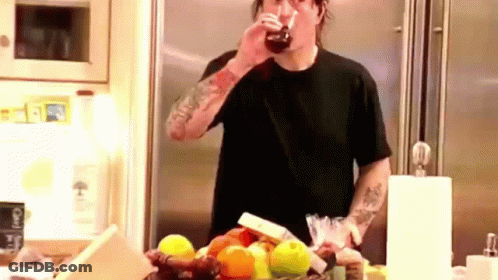 A Man In A Black Shirt Is Drinking A Glass Of Soda In A Kitchen . GIF