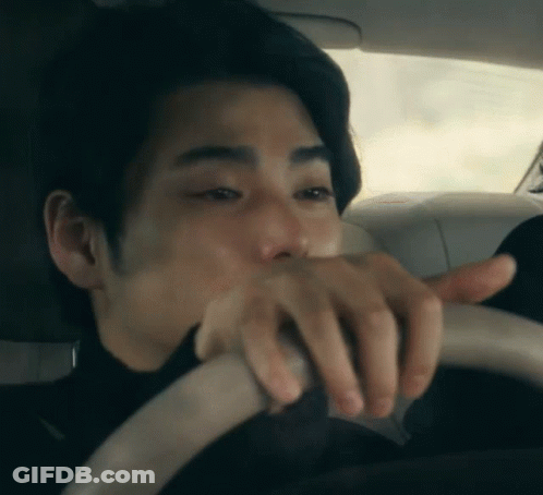 A Man In A Black Shirt Is Driving A Car And Covering His Mouth With His Hand GIF
