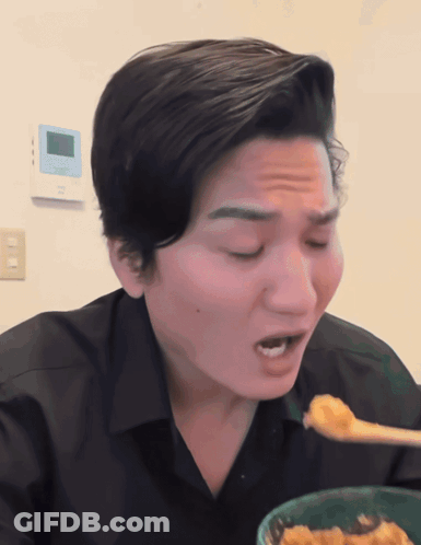 A Man In A Black Shirt Is Eating A Bowl Of Food With A Spoon GIF