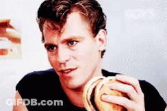 A Man In A Black Shirt Is Eating A Burger GIF