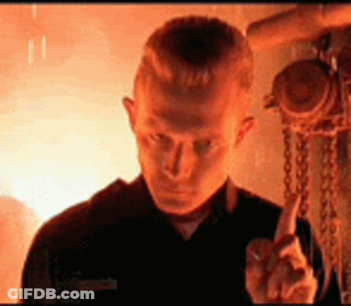 A Man In A Black Shirt Is Giving The Middle Finger In Front Of A Fire . GIF