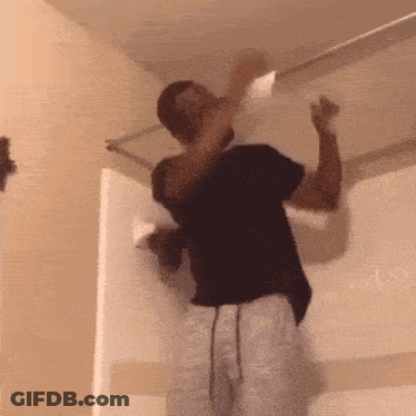 A Man In A Black Shirt Is Hanging Upside Down From A Ceiling . GIF