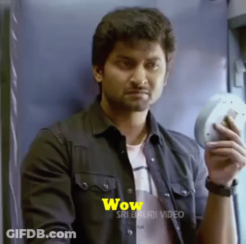A Man In A Black Shirt Is Holding A Cell Phone In His Hand And Making A Surprised Face . GIF