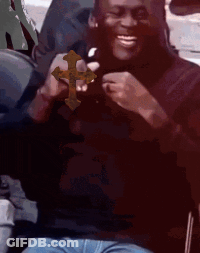 A Man In A Black Shirt Is Holding A Cross In His Hands And Smiling GIF