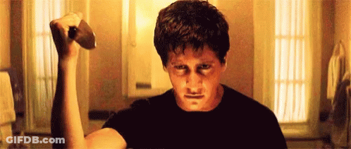 A Man In A Black Shirt Is Holding A Hammer In His Hand . GIF