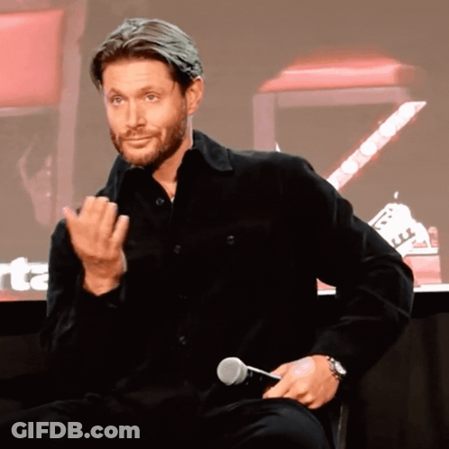 A Man In A Black Shirt Is Holding A Microphone And Making A Face GIF