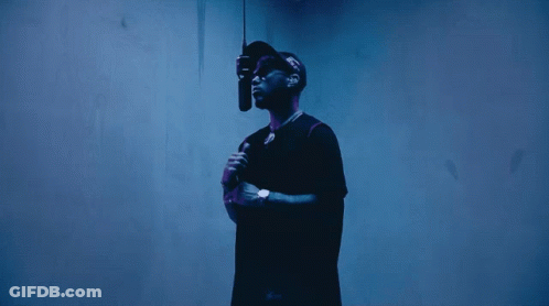 A Man In A Black Shirt Is Holding A Microphone In Front Of A Blue Wall GIF