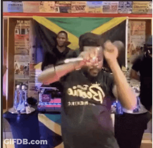 A Man In A Black Shirt Is Holding A Microphone In Front Of A Flag . GIF