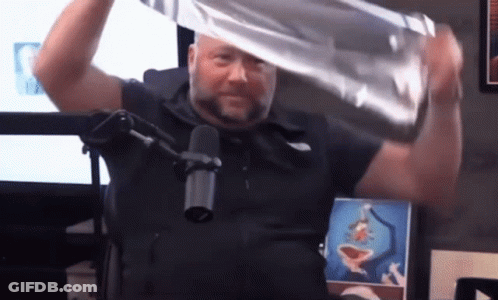 A Man In A Black Shirt Is Holding A Piece Of Aluminum Foil Over His Head In Front Of A Microphone GIF
