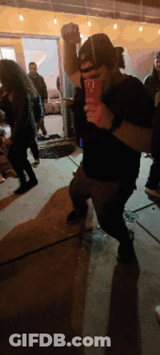 A Man In A Black Shirt Is Holding A Red Cup With The Letter T On It GIF