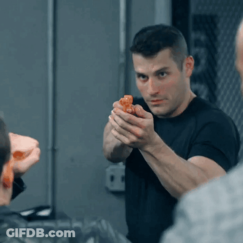 A Man In A Black Shirt Is Holding A Small Orange Object In His Hand GIF