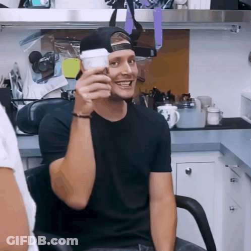 A Man In A Black Shirt Is Holding A White Cup GIF