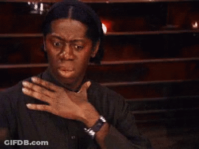 A Man In A Black Shirt Is Holding His Chest With His Hand . GIF