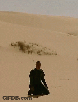 A Man In A Black Shirt Is Kneeling In The Sand GIF